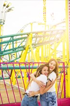 Two happy female friends hugging each other front roller coaster ride