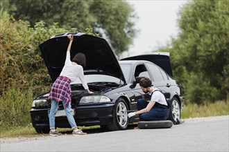 Woman checking engine man swapping tire