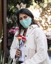 Woman with face mask posing outdoors with flowers