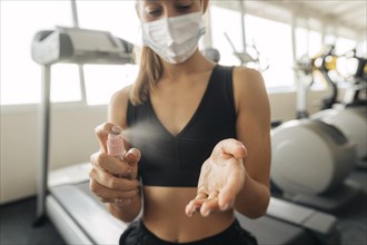 Woman with medical mask gym using hand sanitizer