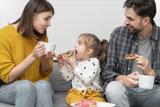Young couple with child eating donuts