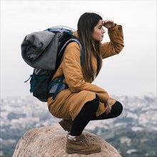 Young female hiker sitting top rock with her backpack eye shielding
