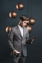 Young man holding disposable coffee cup looking digital tablet standing front streamlined mirror round copper chandelier