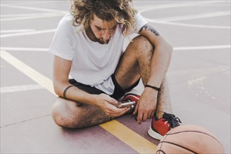 Basketball player sitting court using mobile phone