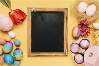 Blank blackboard with fresh flowers decorated easter eggs yellow backdrop