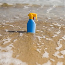 Blue sunscreen plastic bottle shallow sea water beach