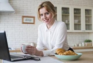 Cheerful business woman with coffee using laptop