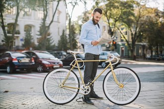 Cheerful man reading newspaper near bike