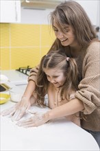 Cheerful mother daughter putting flour table