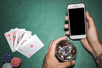 Close up hand holding cellphone whisky glass poker table