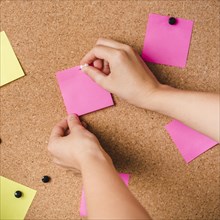 Close up person fixing pink adhesive note with thumbtack corkboard