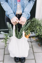 Close up woman s hand holding cotton bag with vegetables