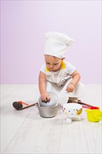 Cook child sitting with kitchen utensils floor