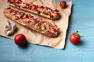 Delicious baguette pizza cherry tomato garlic brown paper blue concrete backdrop