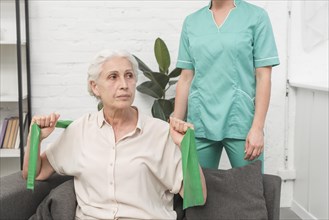 Elderly woman exercising with green stretch band sitting front female nurse