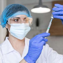 Female researcher with safety glasses medical mask holding syringe vaccine