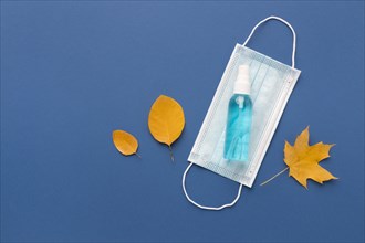 Flat lay medical mask with hand sanitizer autumn leaves
