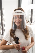 Front view make up artist with face shield holding brushes