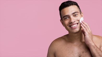 Front view smiley shirtless man using cotton pads his face