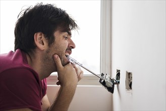 Funny electrician installing plug with screwdriver carrying mouth