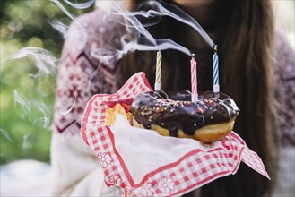 Girl holding chocolate donut with extinguish candles