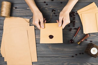 High angle view woman showing seal brown envelop with craft material wooden table