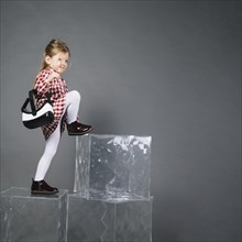 Little girl holding virtual reality glasses climbing transparent blocks against gray background