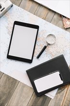 Overhead view digital tablet cell phone magnifying glass diary map against wooden backdrop