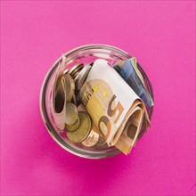 Overhead view euro banknotes coins open glass jar against pink background