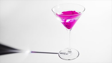 Pink ink dissolving martini glass isolated white backdrop
