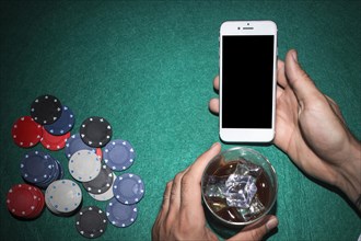 Poker player s hand showing mobile phone holding whiskey glass poker table