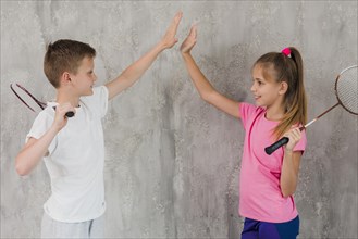 Side view boy girl holding racket hand giving high five standing against wall