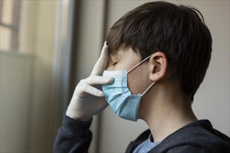 Side view boy with medical mask touching his face