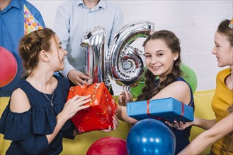 Smiling portrait birthday girl with number 16 foil balloon presents