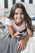 Smiling portrait girl lying bed using remote control