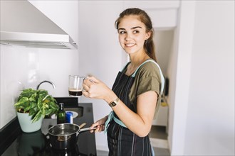 Smiling woman boiling water sauce pan holding coffee cup
