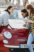 Smiling women with smartphone near man looking map car hood