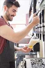 Smiling young male bartender pours fresh light beer from tap