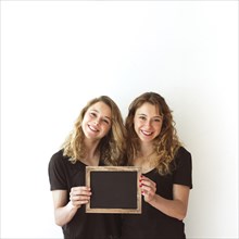 Smiling young sister together holding blank slate isolated white backdrop