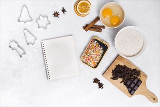 Spiral notepad with colorful sprinkles pastry cutter star anise cinnamon dried citrus egg yolk chocolate bar white backdrop