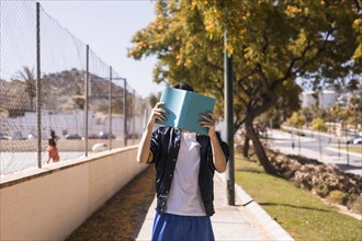 Teenager closing face by book