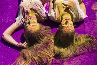 Two young women lying purple holi color powder