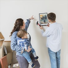 Woman carrying his son directing his husband fix frame wall