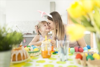 Woman kissing daughter decorating easter eggs