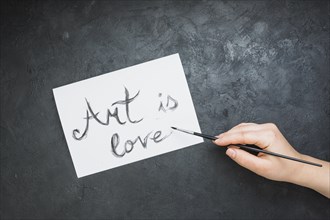 Woman s hand written art is love text white paper with paintbrush slate backdrop