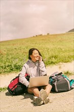 Woman sitting road smiling talking mobile phone among backpacks