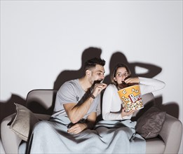 Young lady watching tv eating popcorn near guy settee