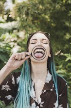 Young woman showing tongue through magnifying glass