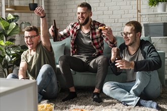 Front view cheerful male friends having pizza with beer watching sports tv