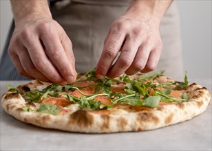 Front view man putting arugula baked pizza dough with smoked salmon slices